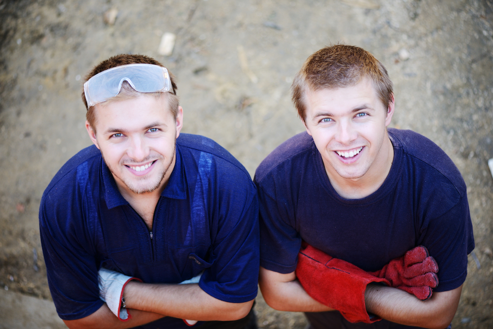 Two male construction twin workers smiling at a building site